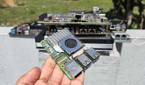 A person holding a Raspberry Pi in front of other SBCs, mini-PCs, and NAS