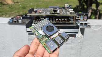 A person holding a Raspberry Pi in front of other SBCs, mini-PCs, and NAS