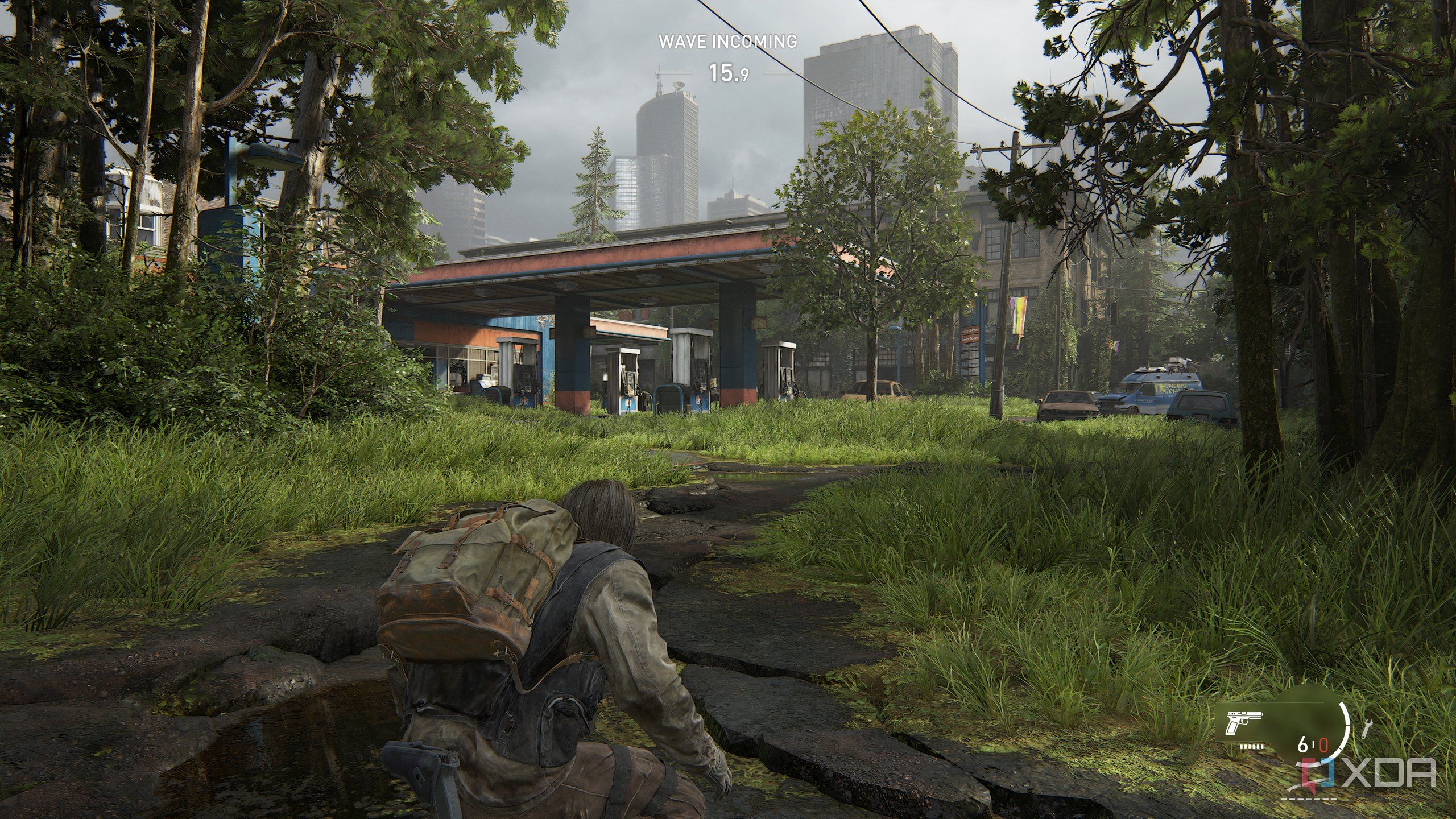 A screenshot from the game The Last of Us Part II Remastered on PC, showing Bill crouching on a broken road, with a gas station nearby.