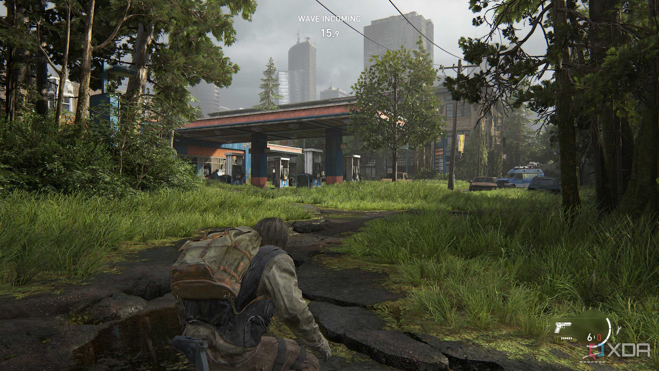 A screenshot from the game The Last of Us Part II Remastered on PC, showing Bill crouching on a broken road, with a gas station nearby.