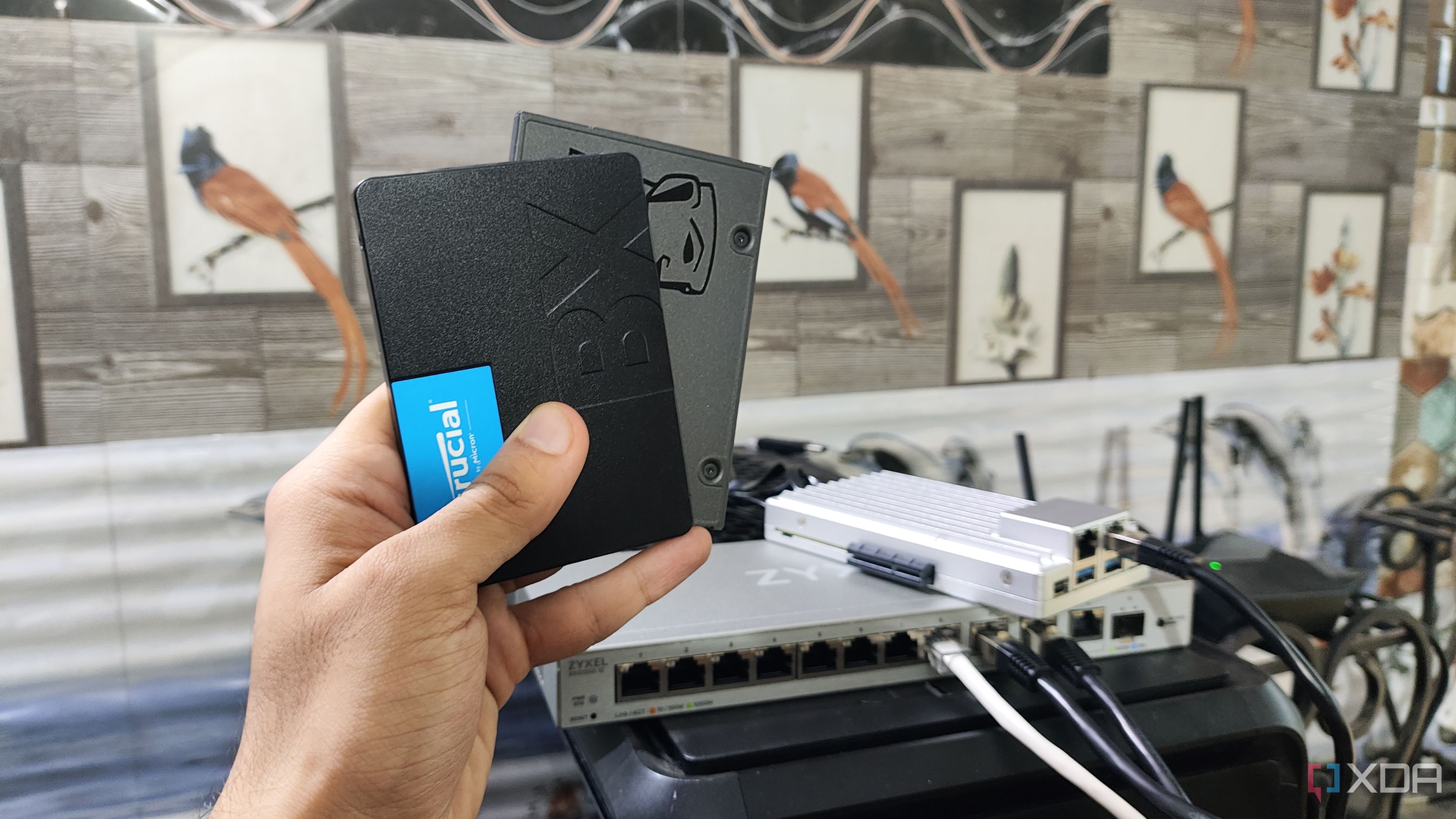 A person holding two SSDs, with a ZimaBoard 2 lying in the background