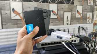 A person holding two SSDs, with a ZimaBoard 2 lying in the background