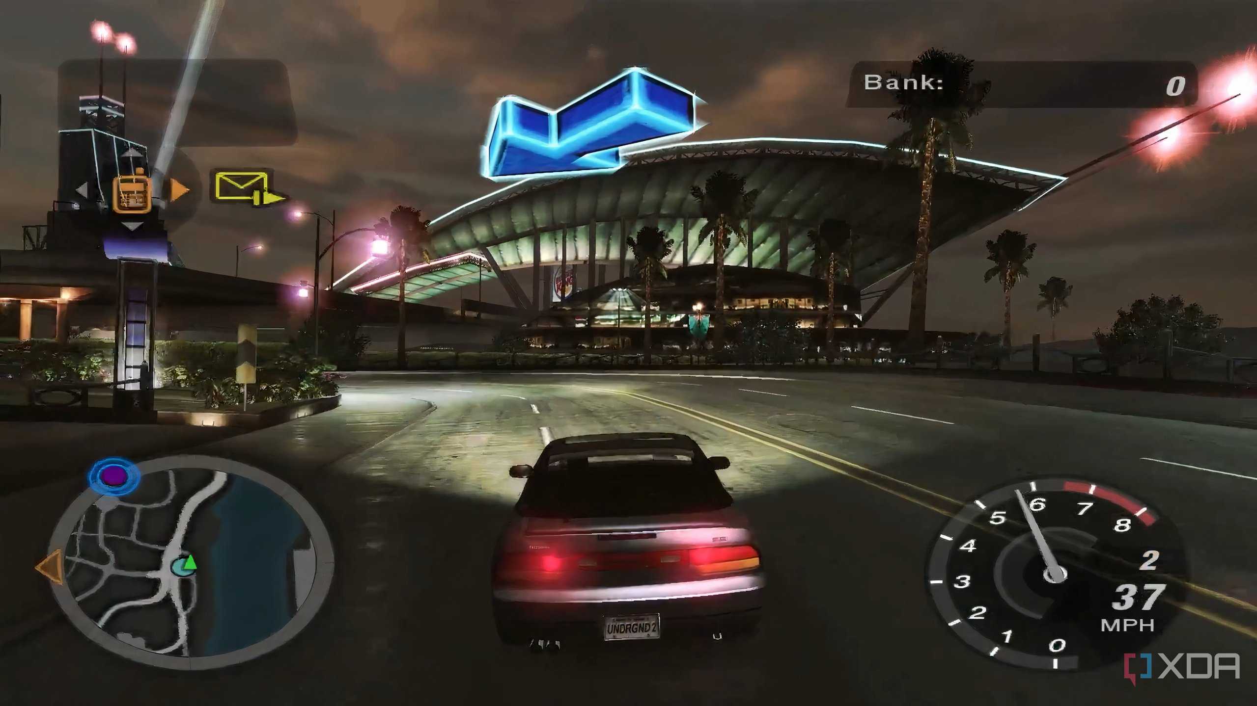A screenshot from the game Need for Speed: Underground 2, showing a car speeding down the road while a big blue arrow points the way forward.