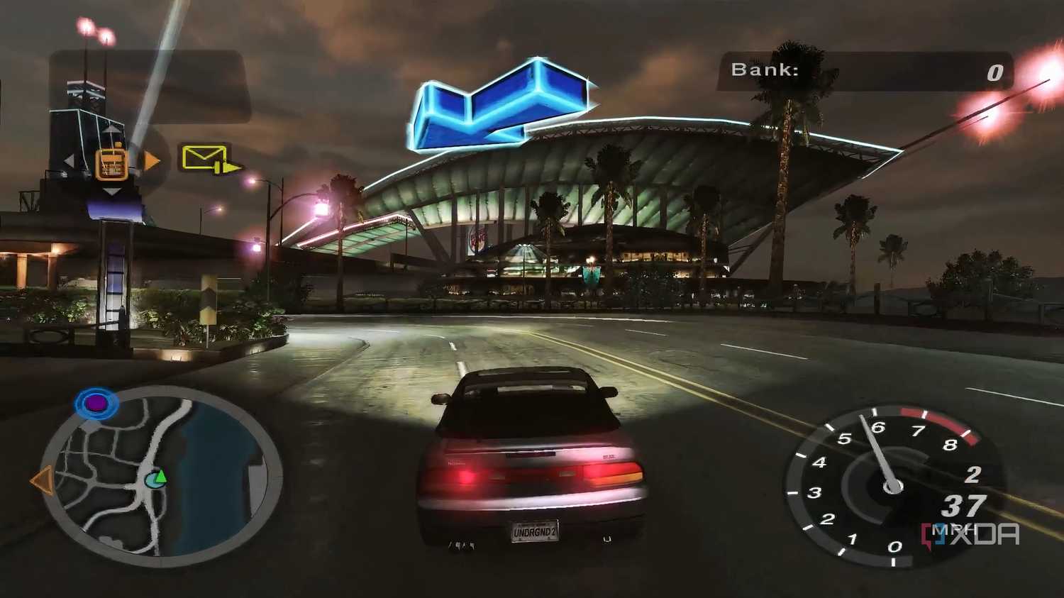 A screenshot from the game Need for Speed: Underground 2, showing a car speeding down the road while a big blue arrow points the way forward.