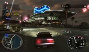A screenshot from the game Need for Speed: Underground 2, showing a car speeding down the road while a big blue arrow points the way forward.