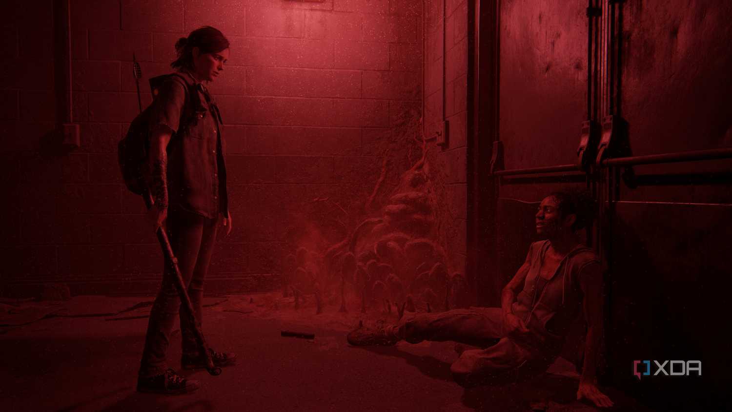 Ellie standing over Nora in a dark, red-lit hallway in The Last of Us Part II.