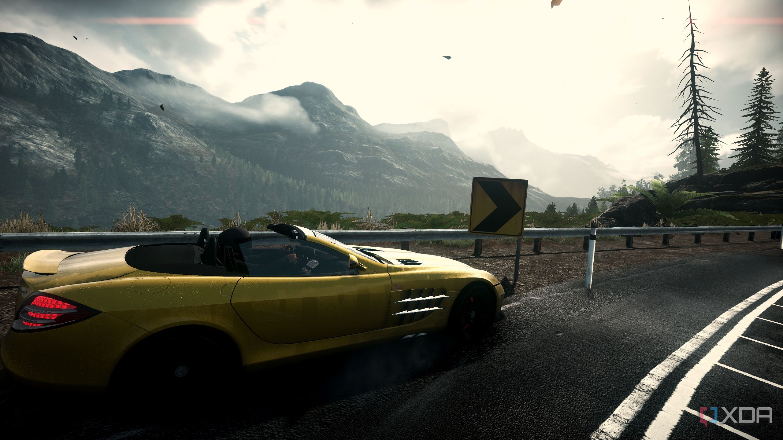 Side shot of a yellow Mercedes convertible riding down a mountain road.