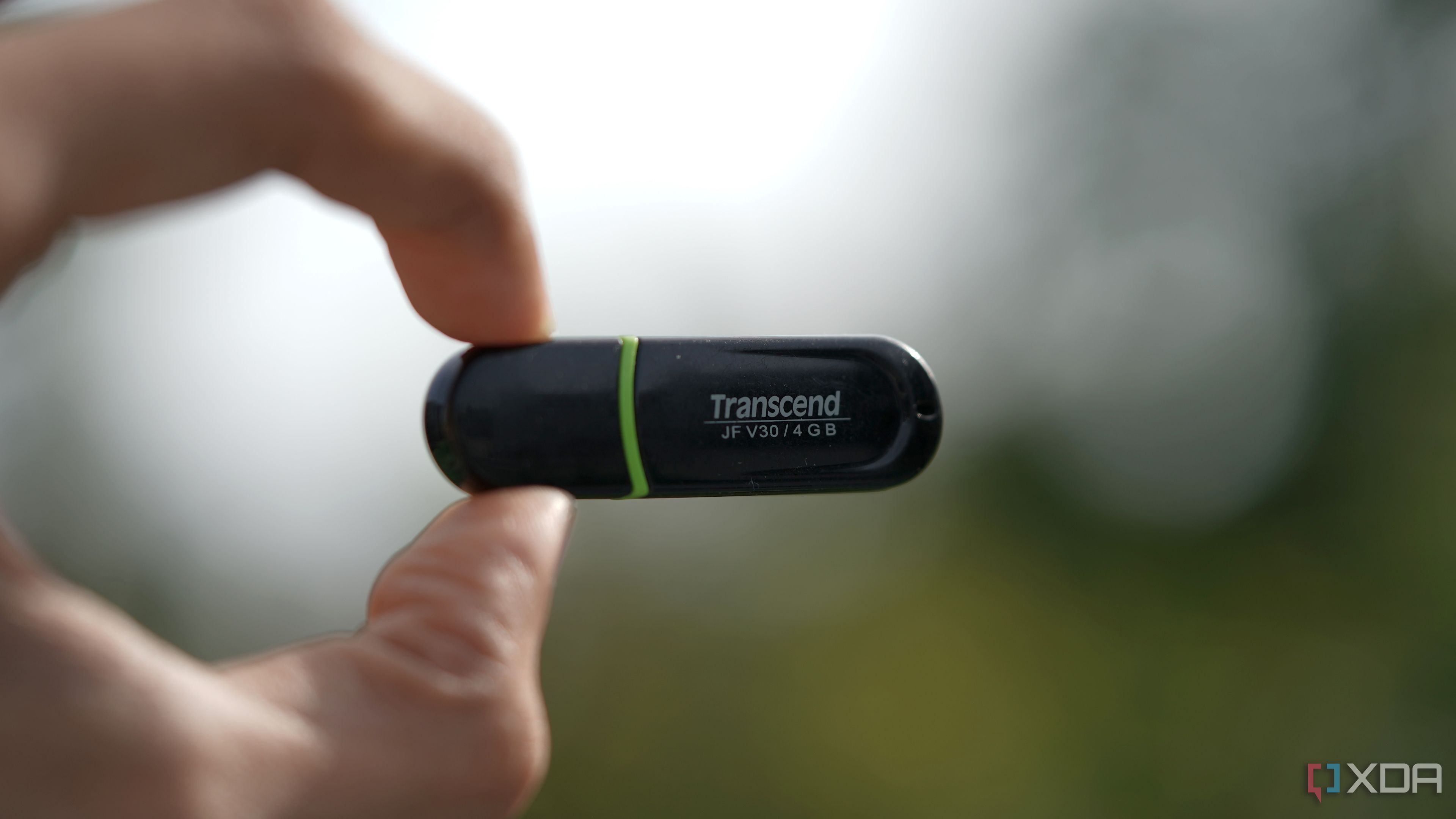 4GB Transcend USB drive held in a pinch against a blurry background