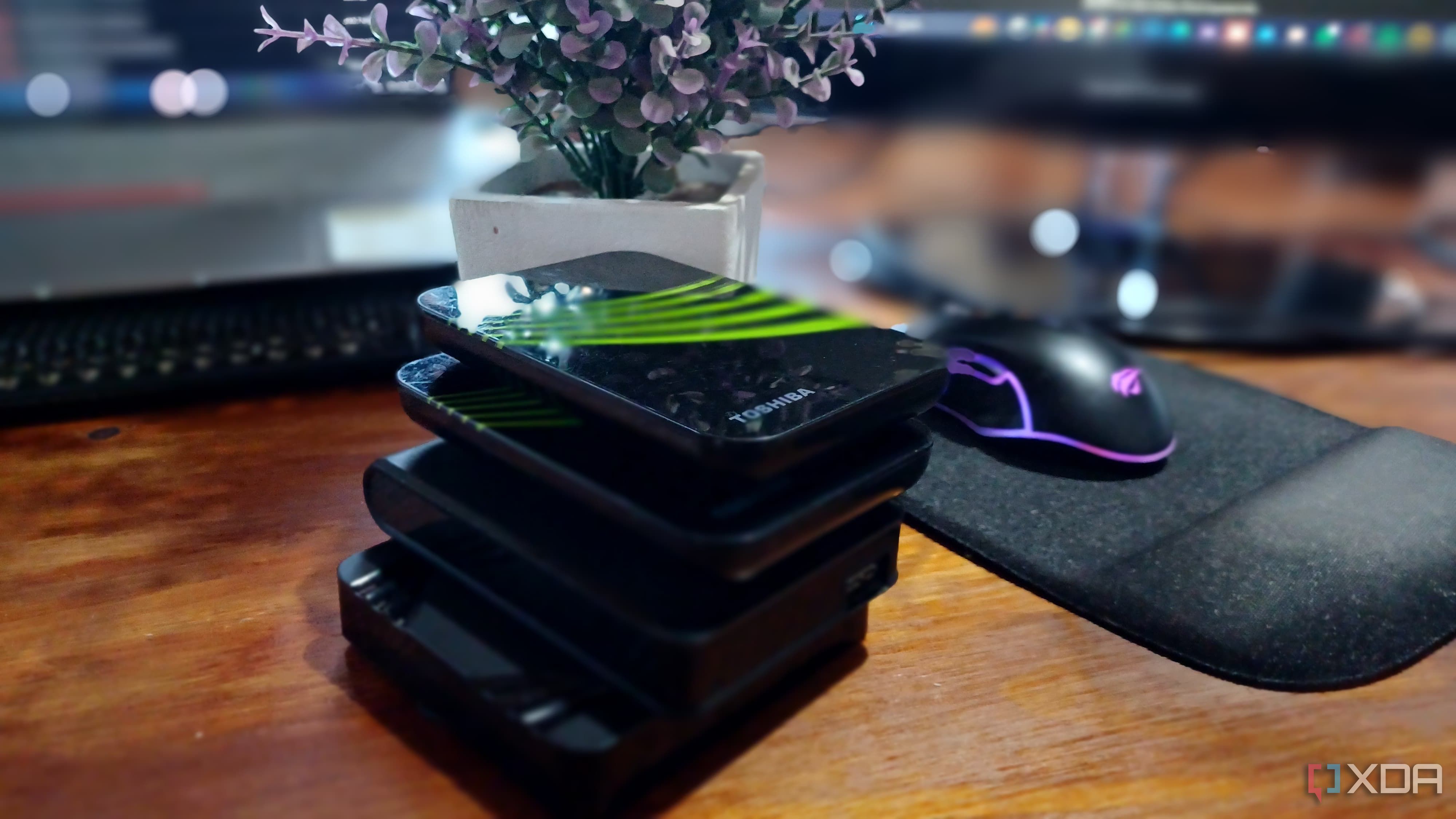 Various external storage devices stacked on top of each other on a wooden tablet with a gaming mouse with lights on the side