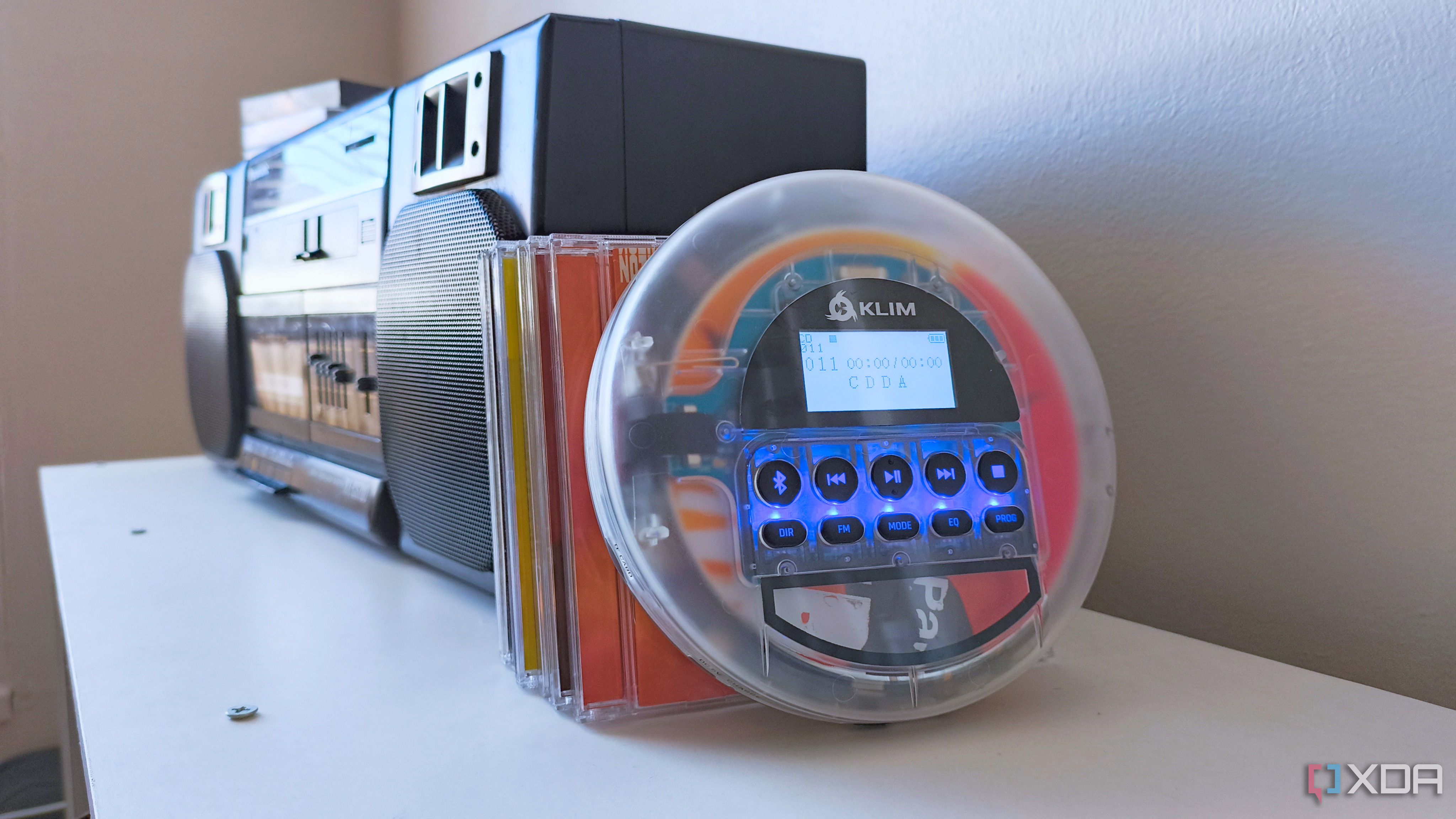 A Klim Nomad CD player propped against a stack of CDs and a Panasonic CD player