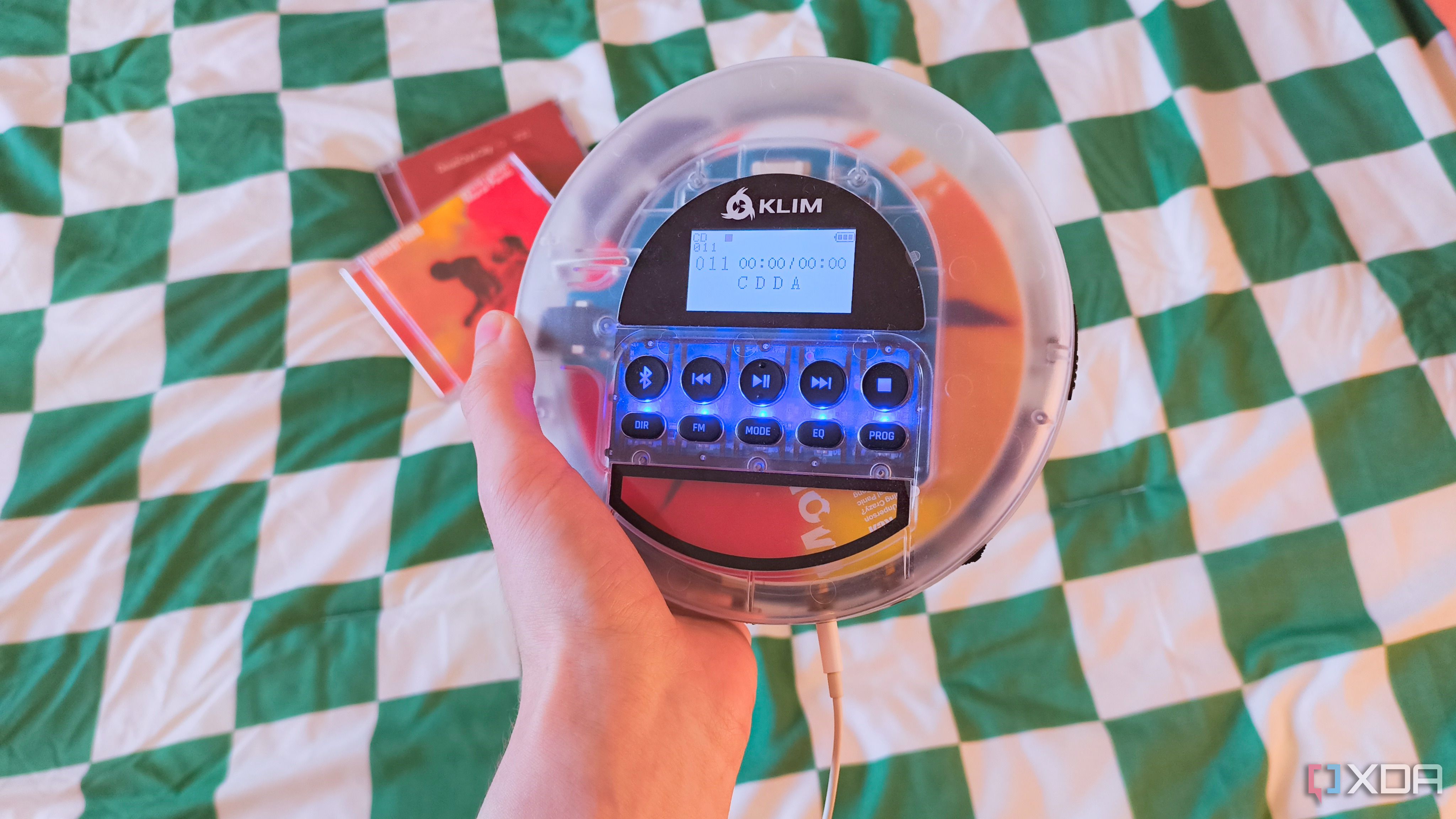A hand holding a Klim Nomad CD player with a Nothing But Thieves CD inside