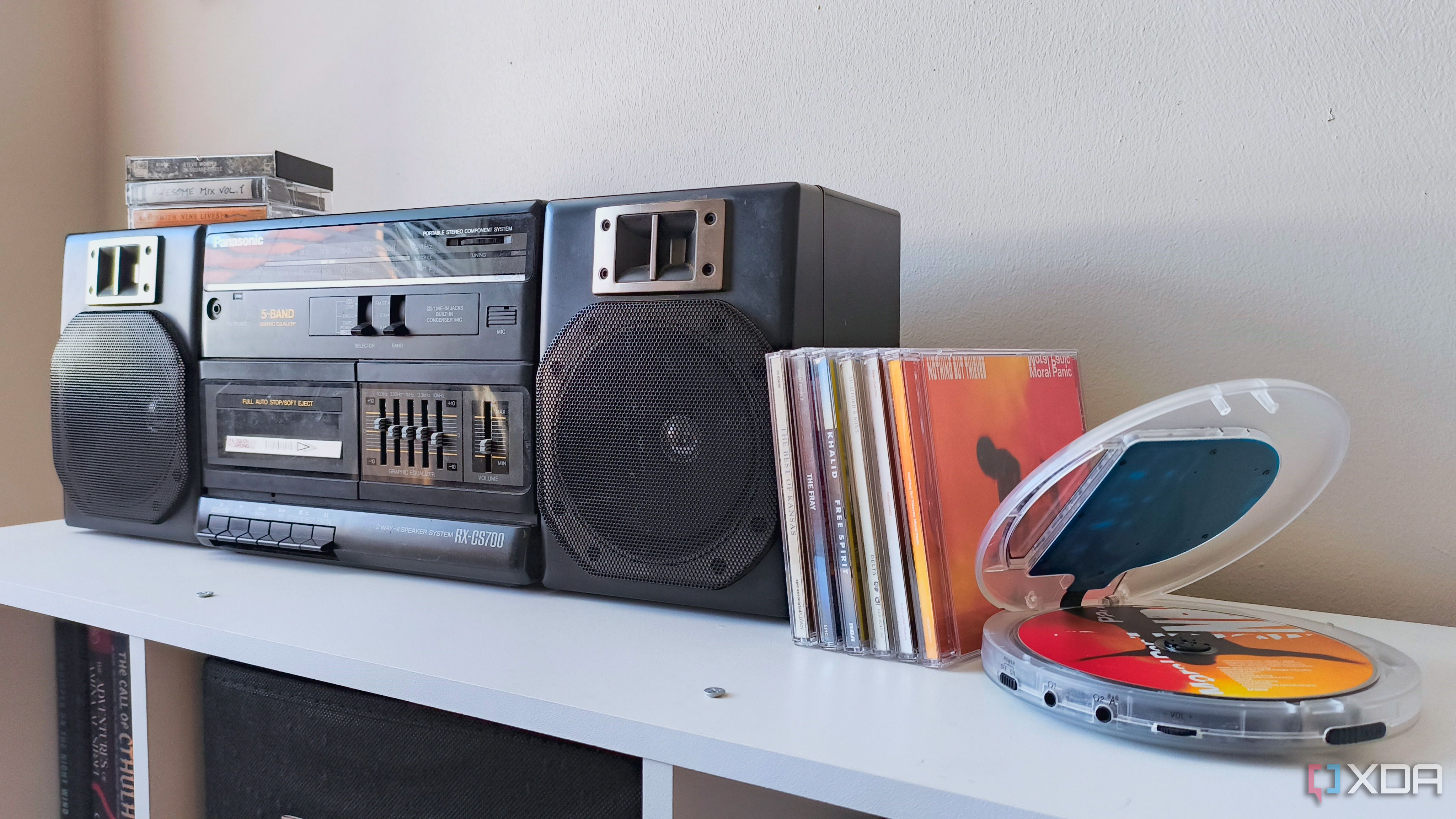 An open Klim Nomad CD player next to a stack of CDs and a Panasonic boom box