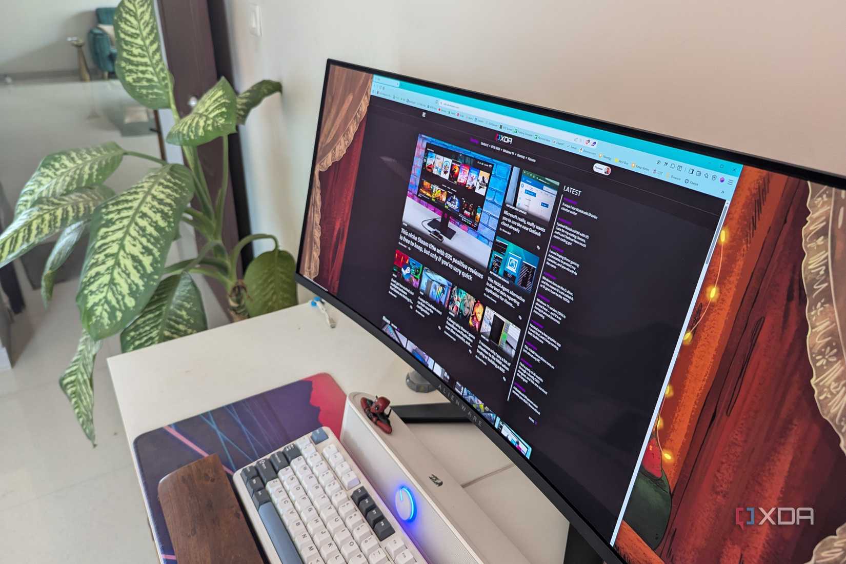 An ultra-wide monitor tilted on the table next to the plant