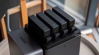 Ugreen DH4300 Plus four-bay hard drive enclosure on a table with blurred wooden chairs in background. Bays numbered 1-4.