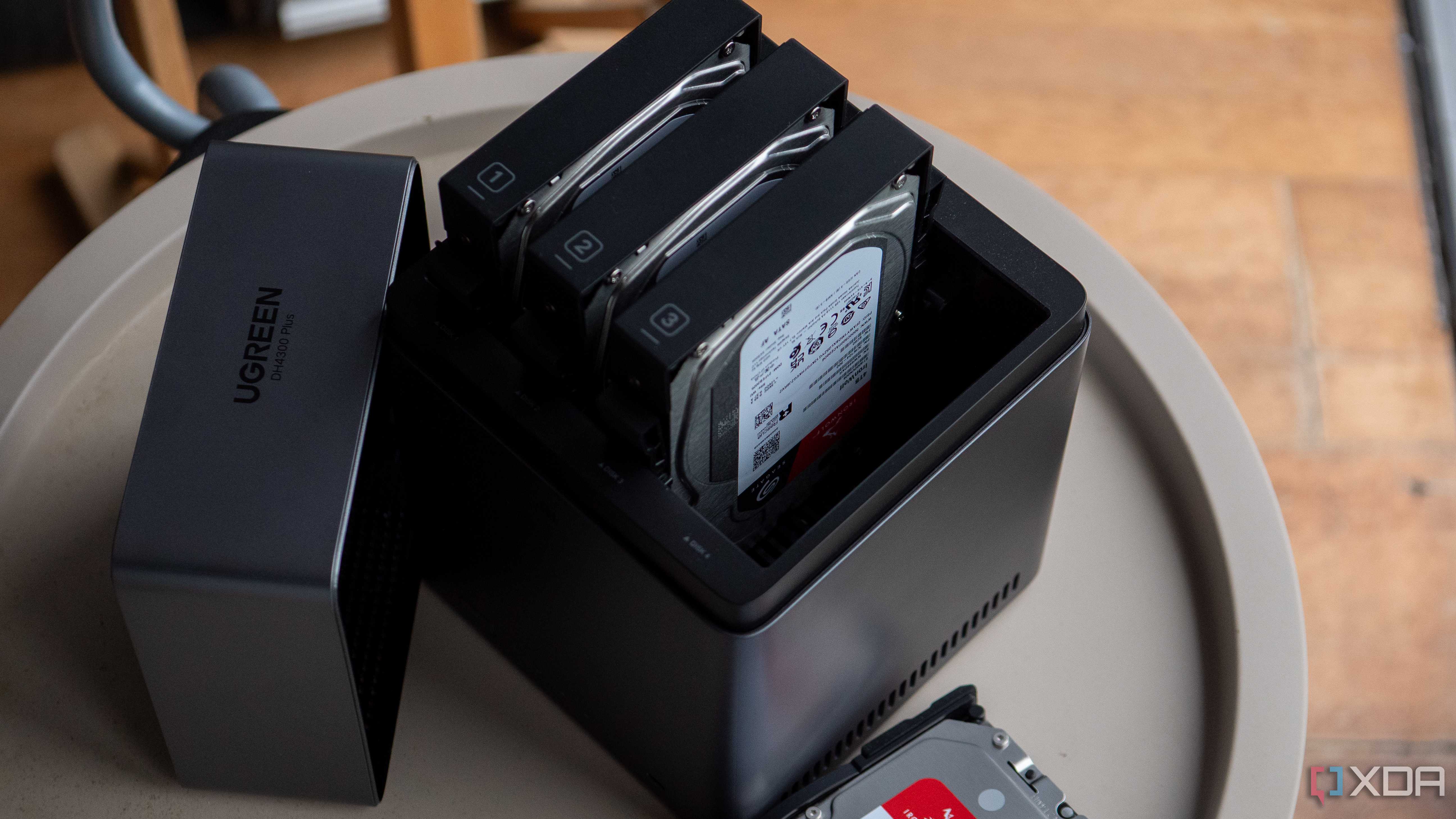 Ugreen DH4300 Plus with three drives inserted on a light beige table. Text reads "UGREEN."