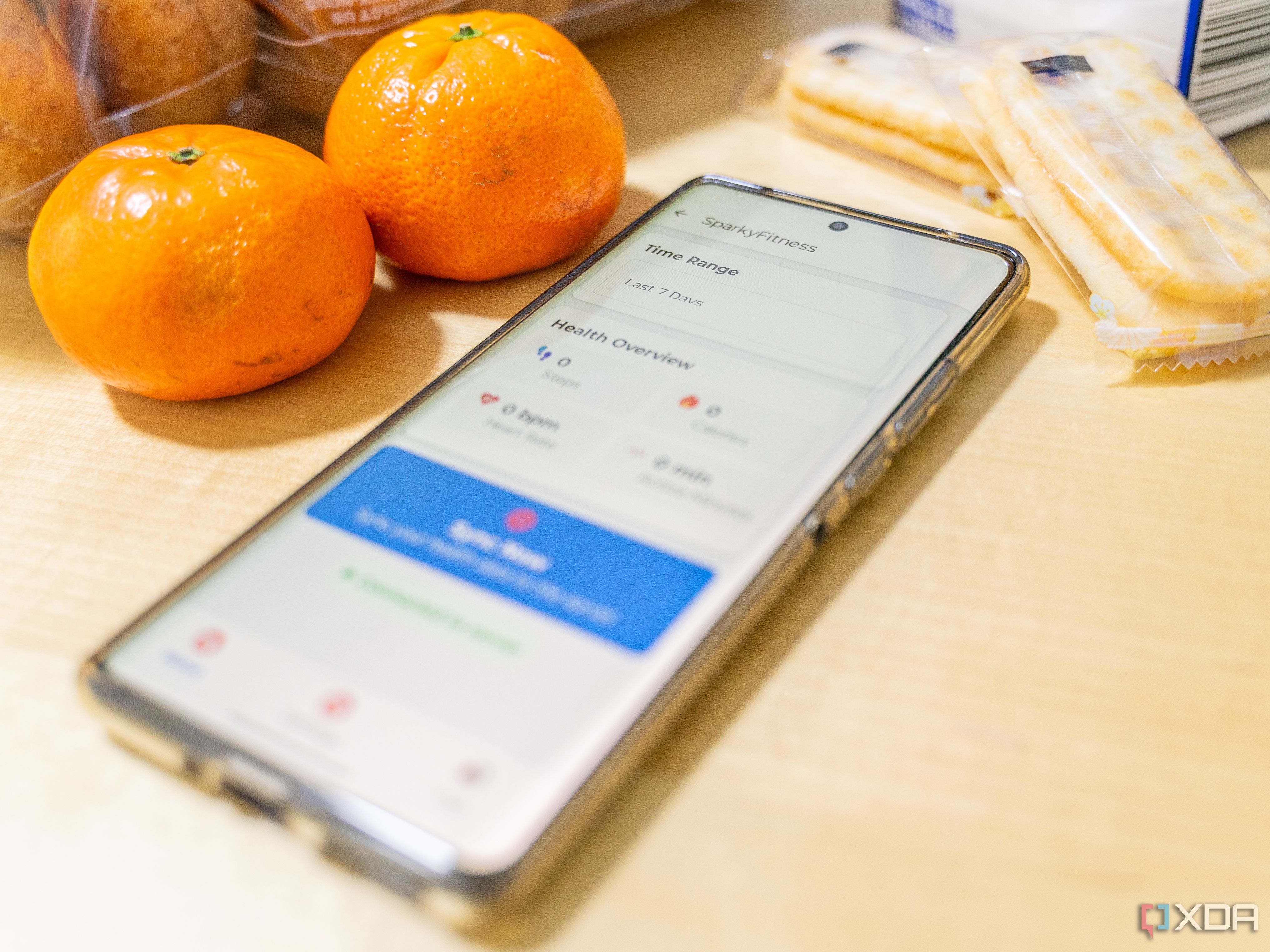 An image of a smartphone surrounded by two oranges, rice crackers and other foods.