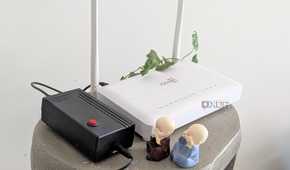 A white home router next to a black mini UPS and two figurines