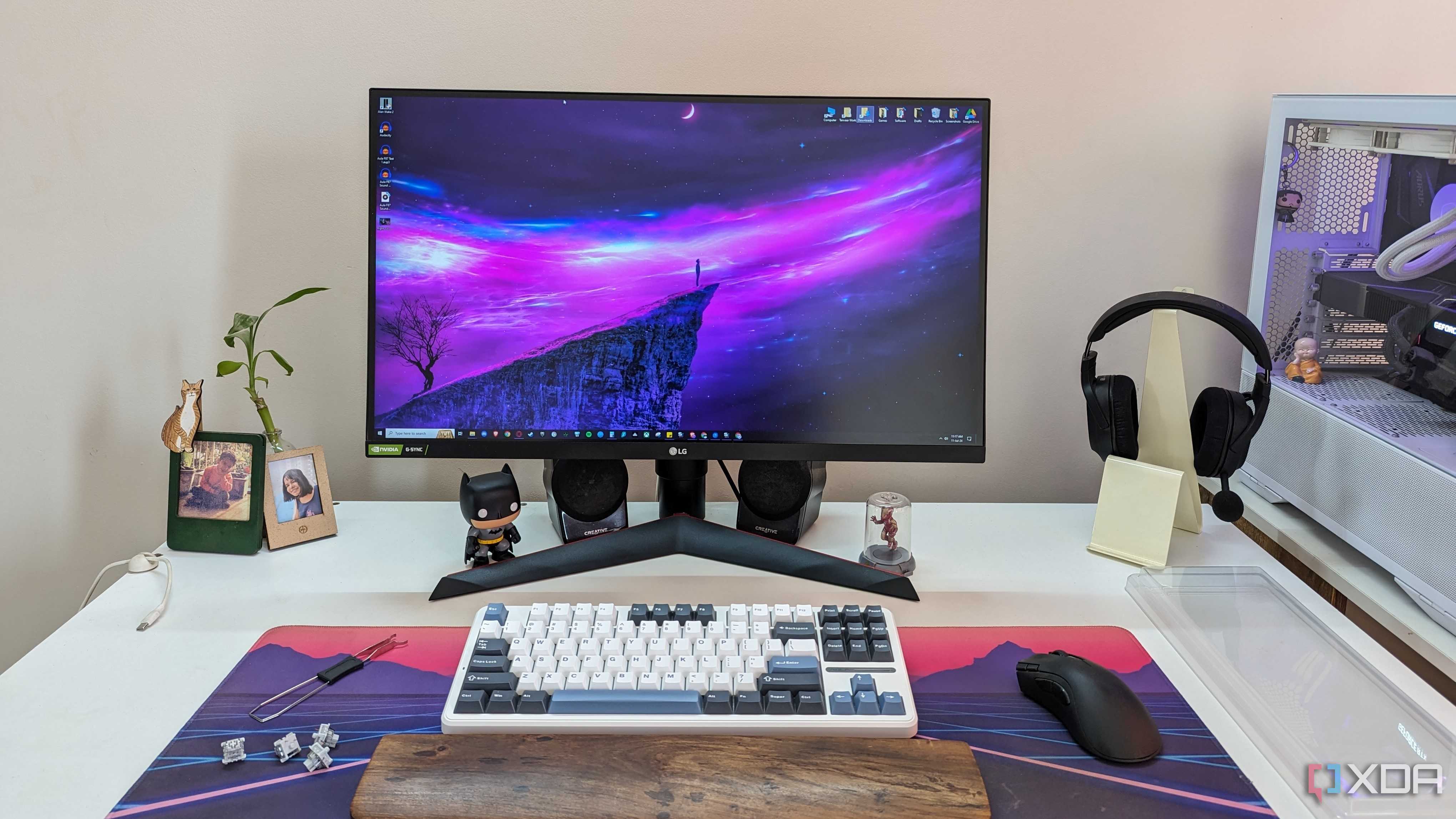 A monitor next to a keyboard, mouse, headphones, and a white PC on a white desk