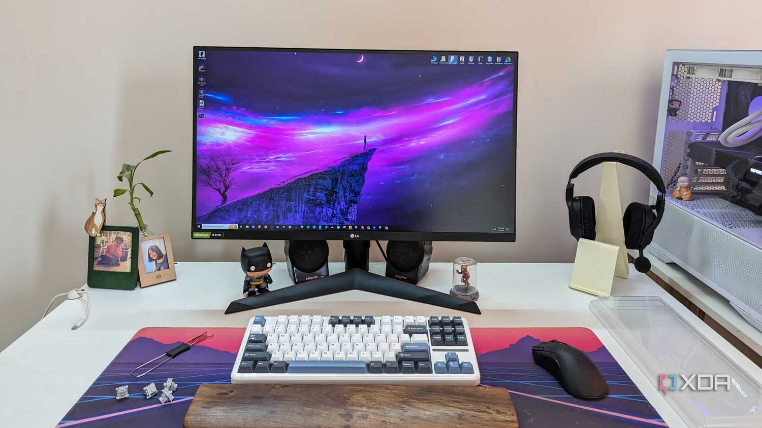 A monitor next to a keyboard, mouse, headphones, and a white PC on a white desk