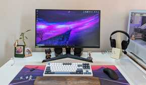 A monitor next to a keyboard, mouse, headphones, and a white PC on a white desk