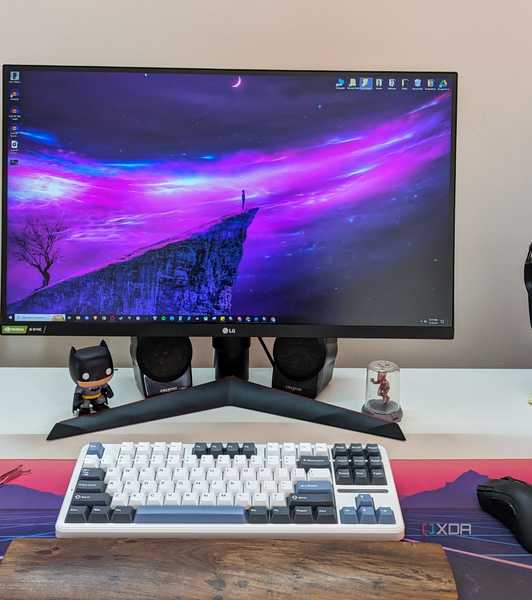 A monitor next to a keyboard, mouse, headphones, and a white PC on a white desk