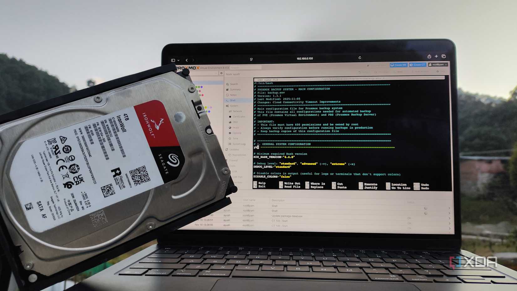 Una persona que sostiene un disco duro frente a una MacBook con la interfaz de usuario web de Proxmox abierta