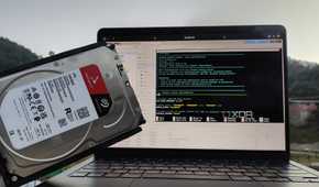 A person holding an HDD in front of a MacBook with Proxmox's web UI open