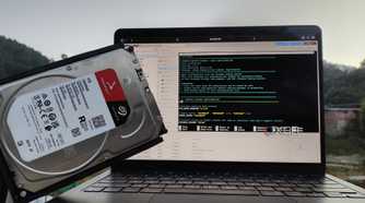 A person holding an HDD in front of a MacBook with Proxmox's web UI open