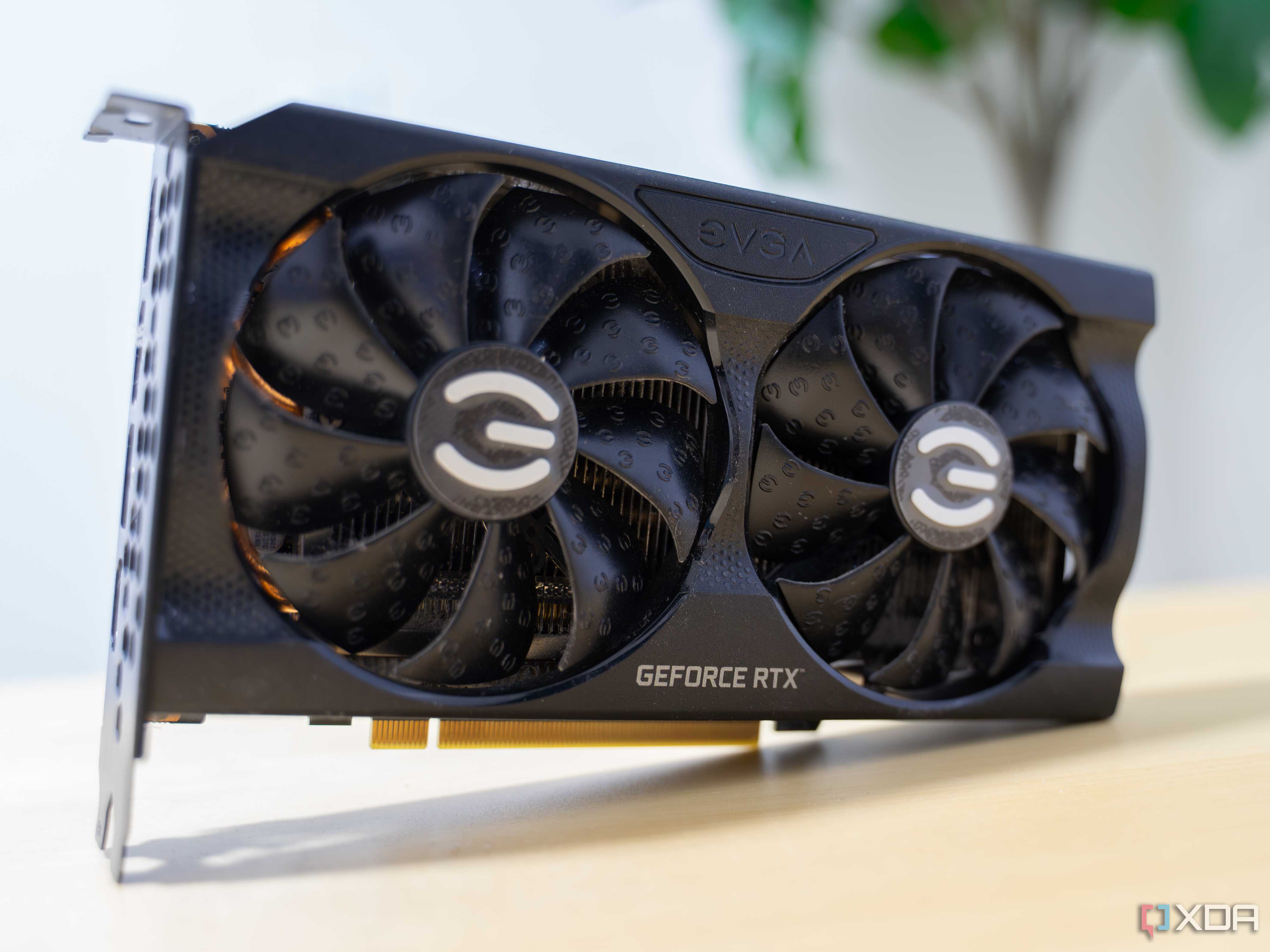 A graphics card with a black shroud standing on its side on a yellow table.