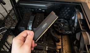 A photo of someone holding a RAM stick in front of a PC with the side panel off