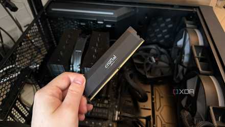 A photo of someone holding a RAM stick in front of a PC with the side panel turned off
