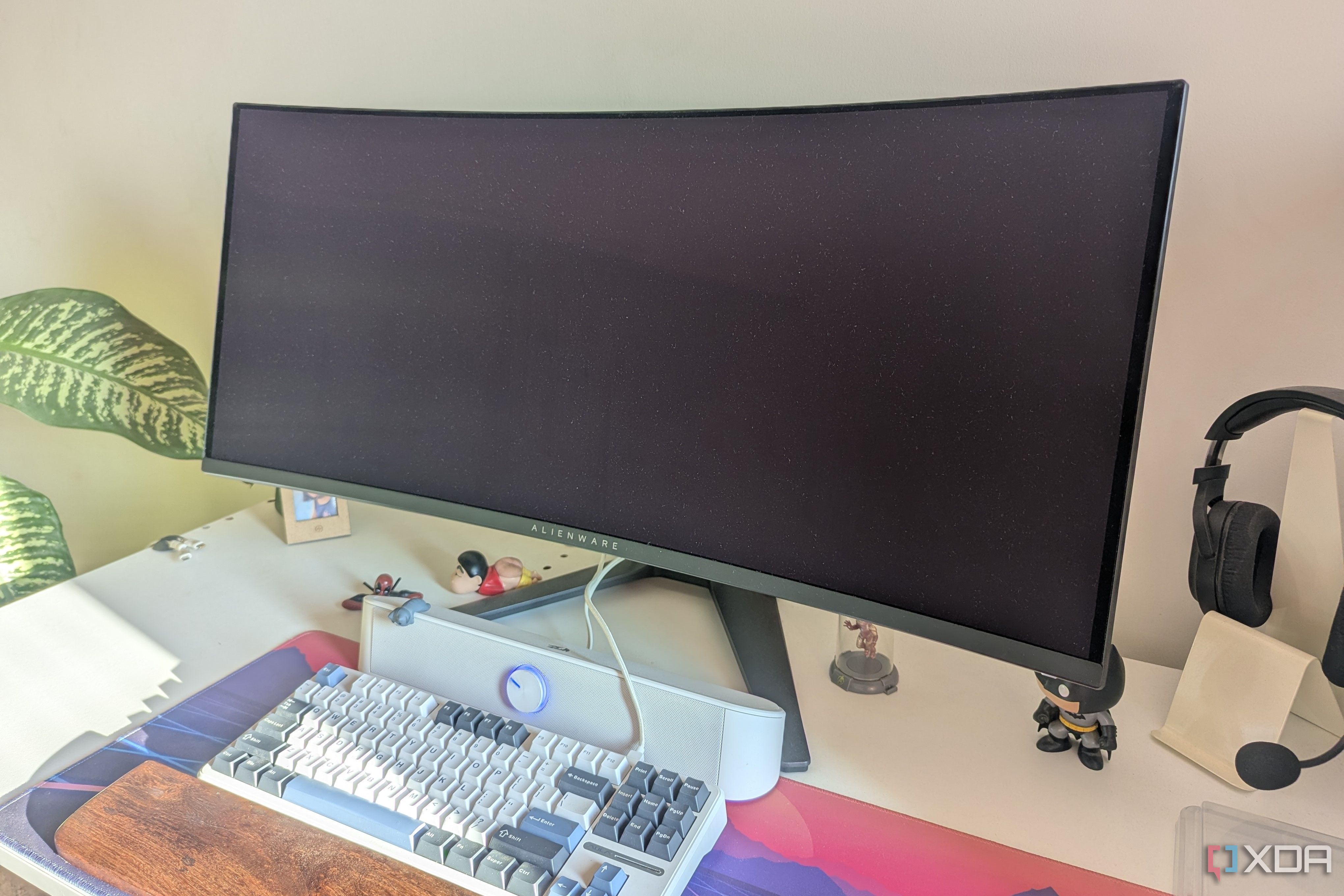 An turned-off ultrawide monitor on a white desk next to a keyboard and soundbar