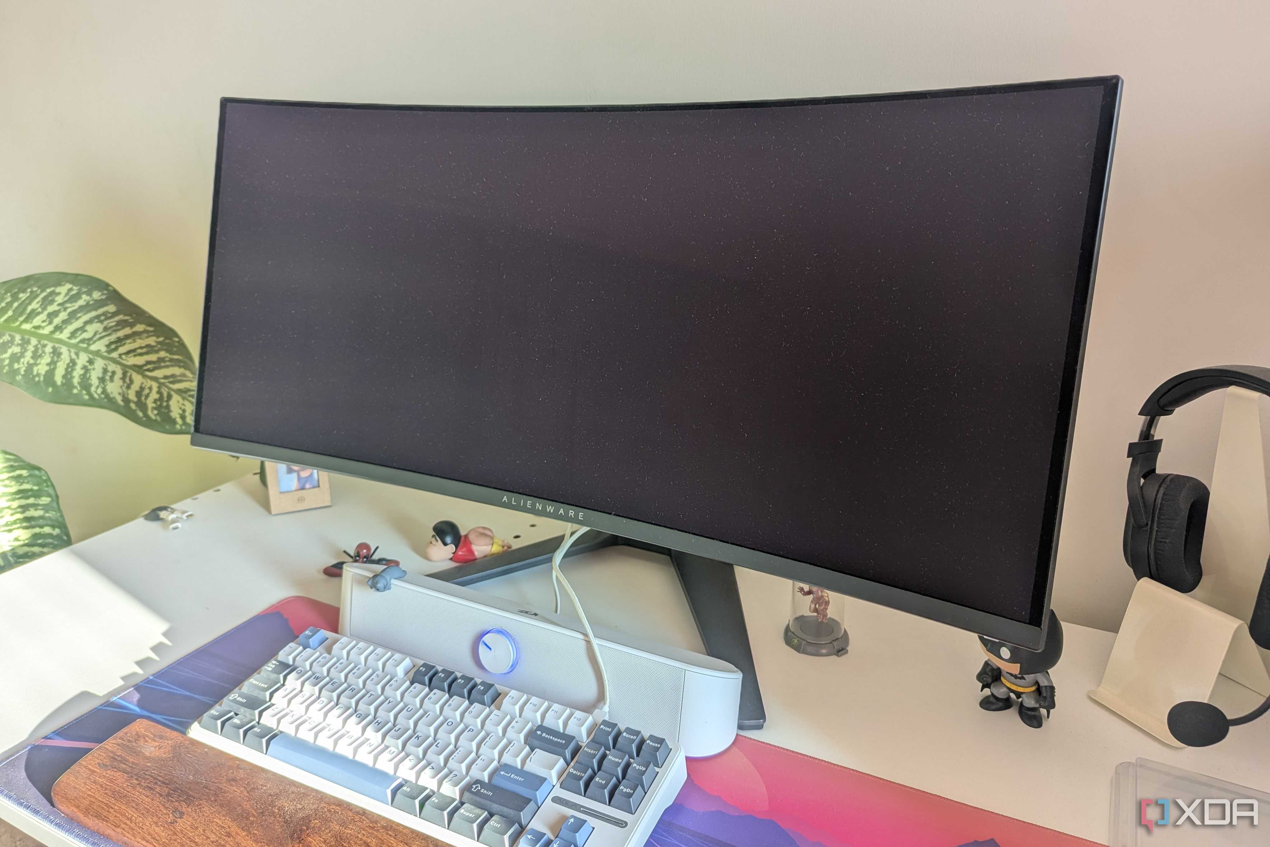 An turned-off ultrawide monitor on a white desk next to a keyboard and soundbar