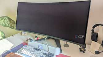 An turned-off ultrawide monitor on a white desk next to a keyboard and soundbar
