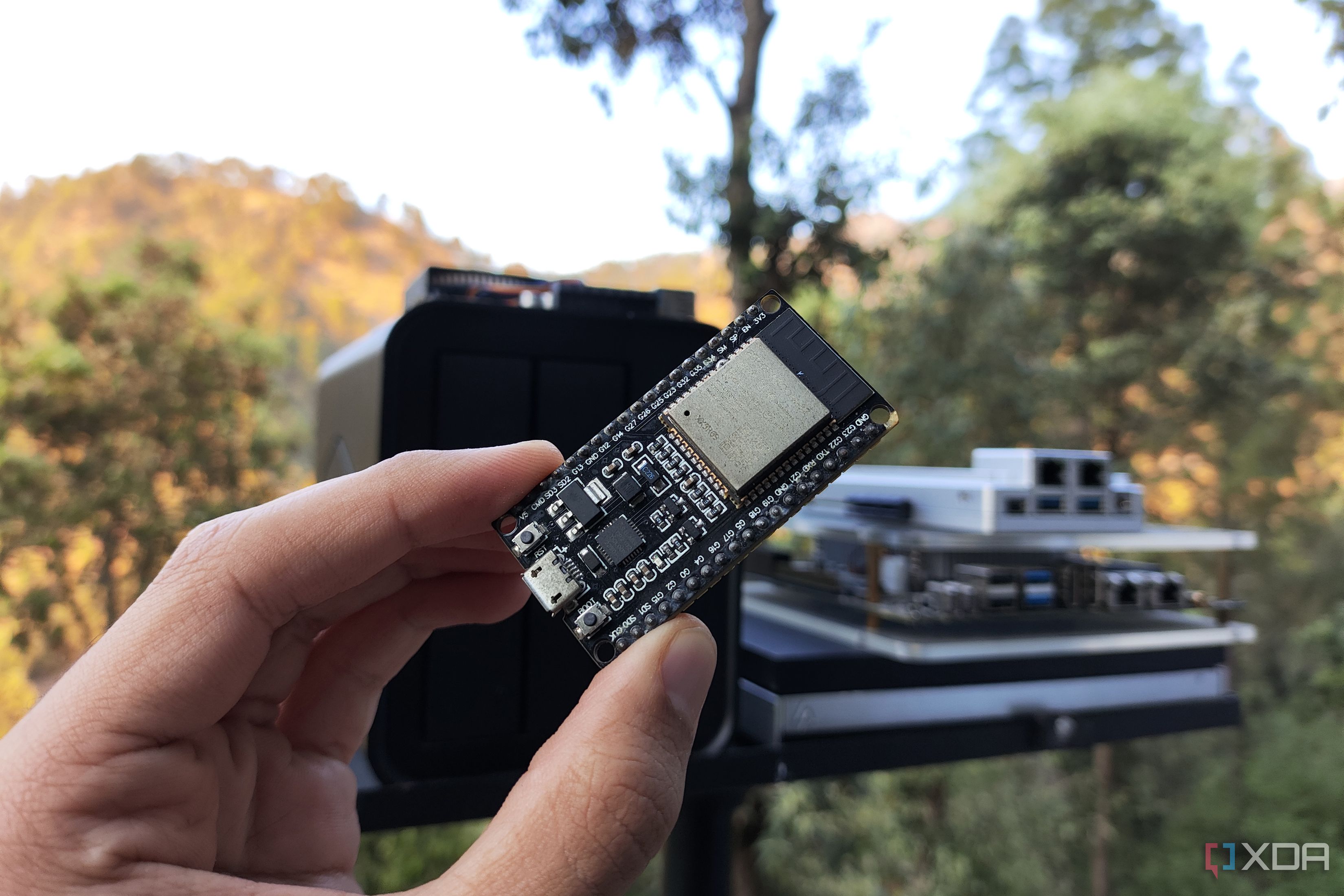 A person holding an ESP32 in front of home lab devices