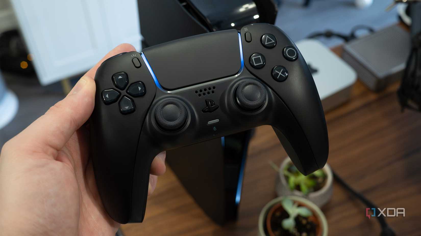 Un controlador de PS5 negro sostenido sobre un escritorio