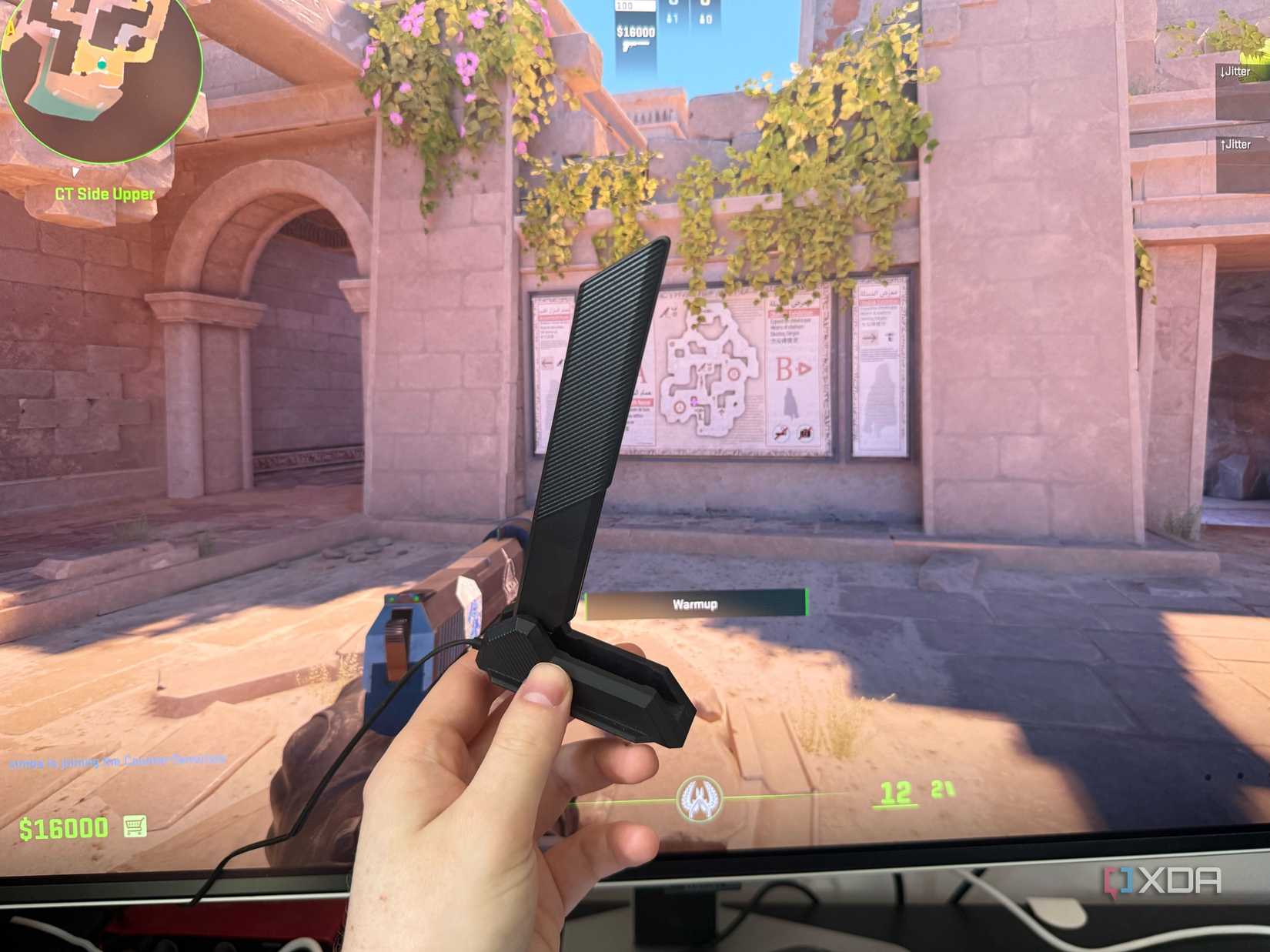 A picture of someone holding a wi-fi antenna in front of a gaming PC monitor displaying CS2