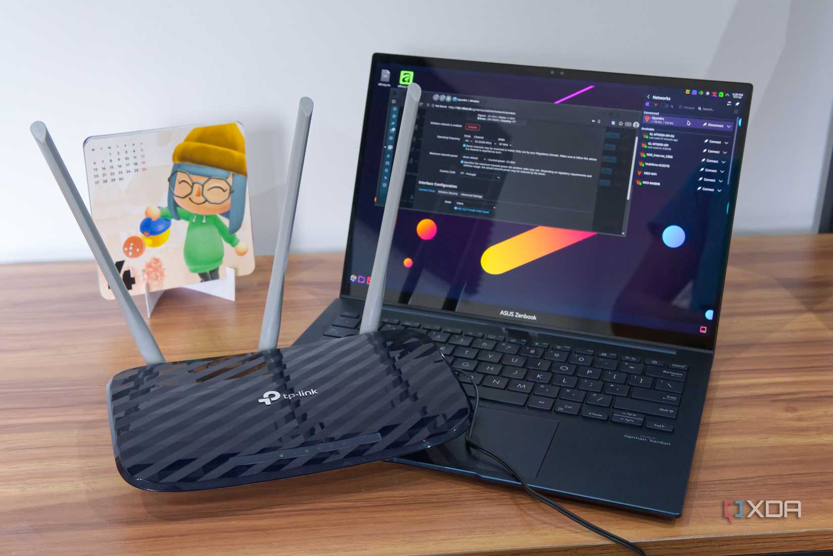 A router next to a laptop displaying a page on the OpenWrt dashboard