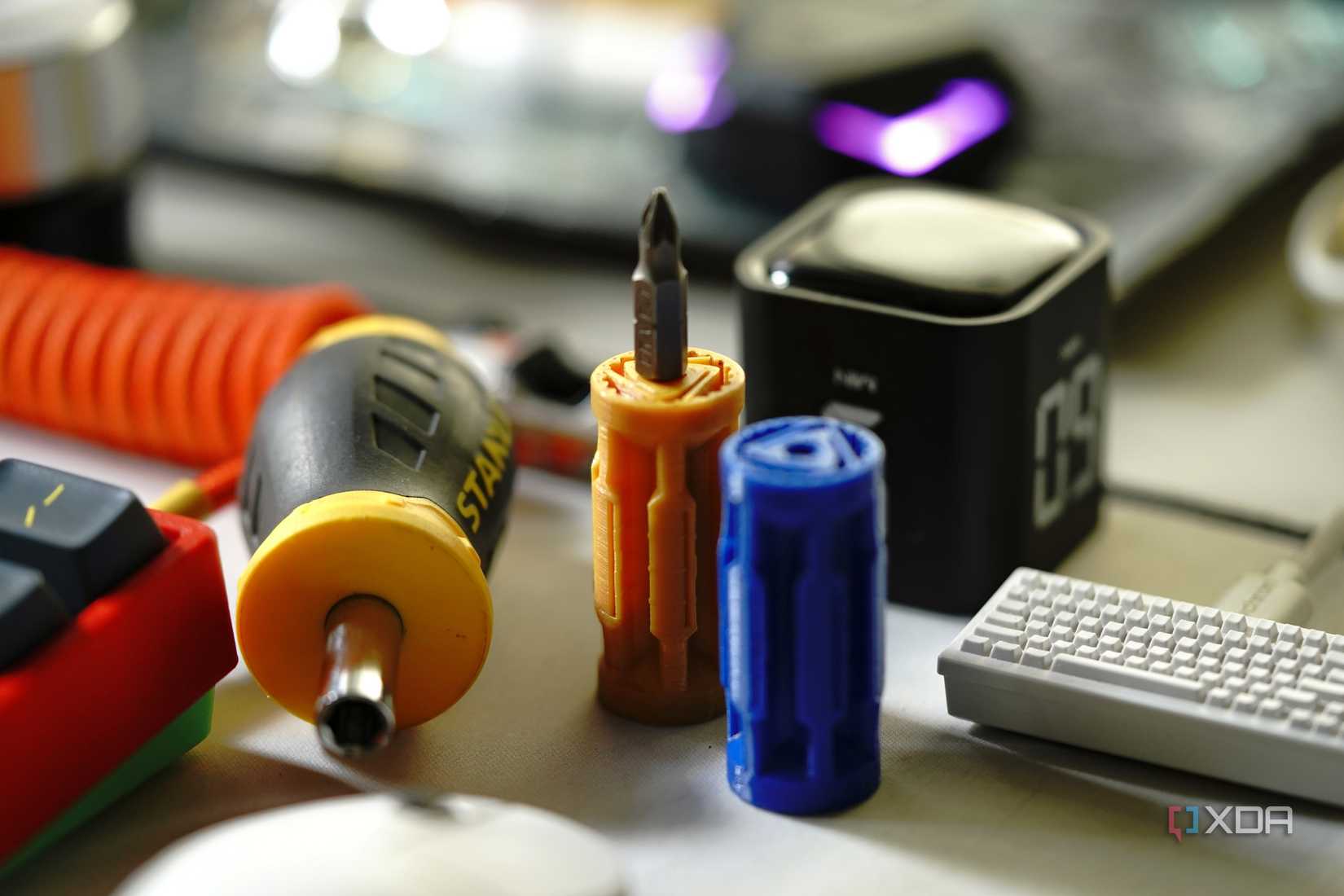 A blue and yellow 3D printed screwdriver beside an actual Stanley screwdriver on a cluttered desk