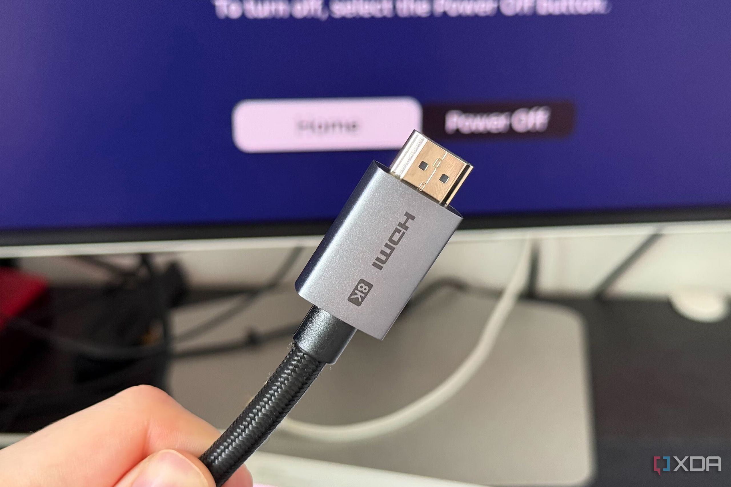 A photo of someone holding an HDMI 2.1 Ultra High Speed cable in front of a display