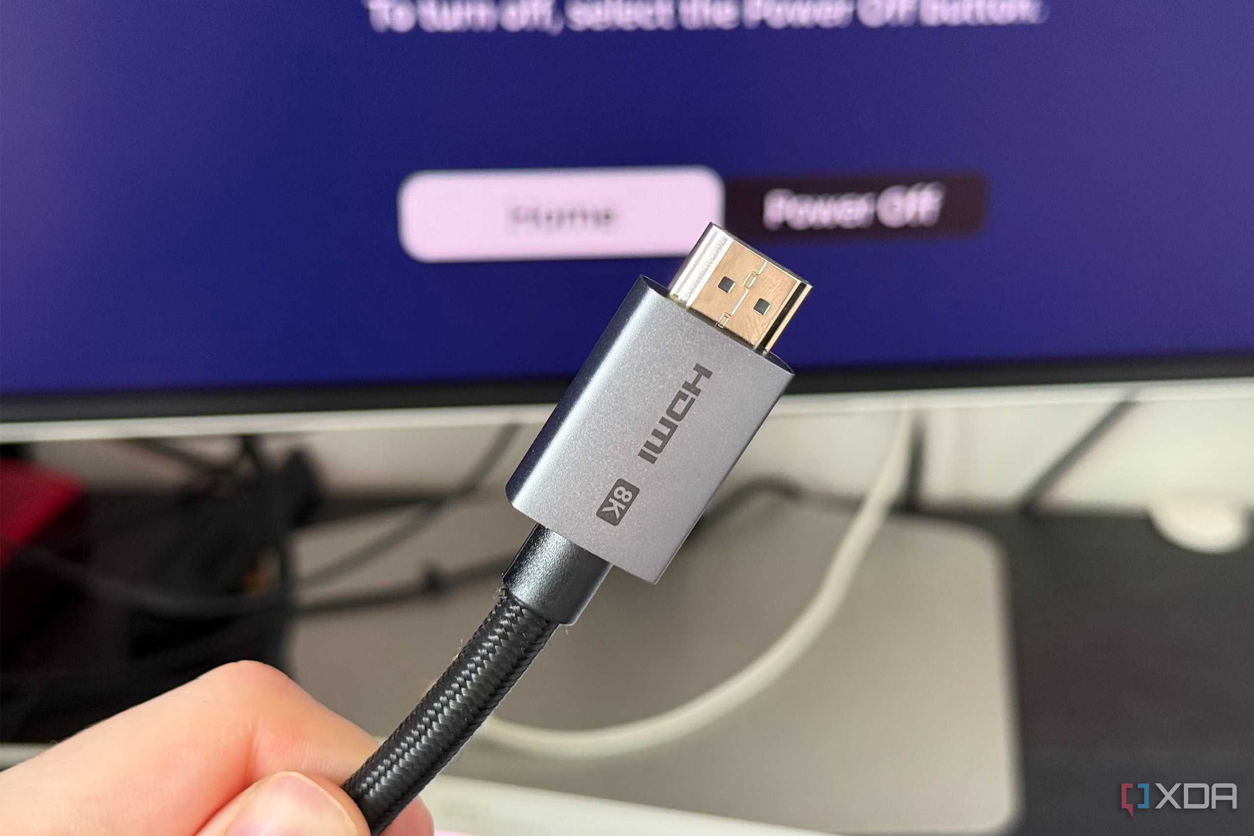 A photo of someone holding an HDMI 2.1 Ultra High Speed cable in front of a display