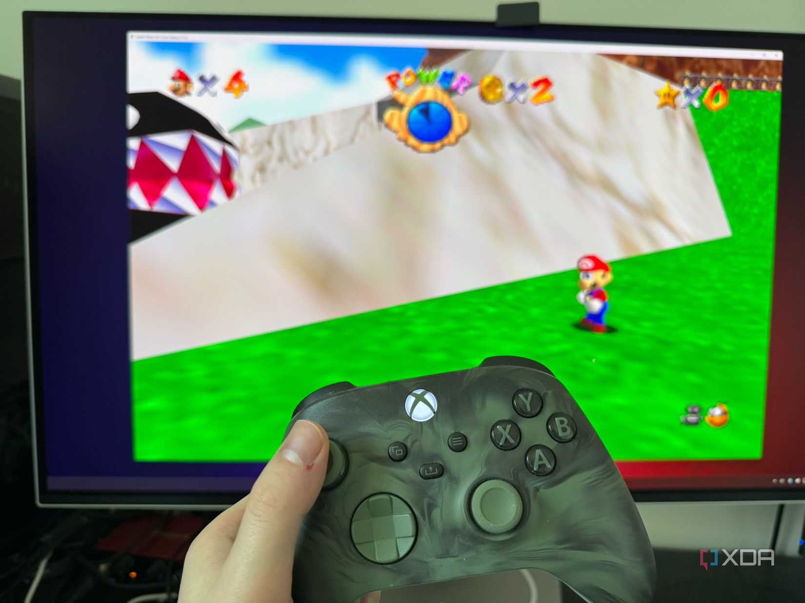 A photo of someone holding an Xbox controller in front of a PC running a native port of SM64.