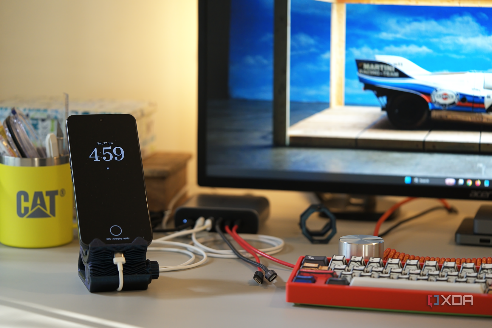 The smartphone sits vertically on a 3D printed stand in front of a computer monitor.