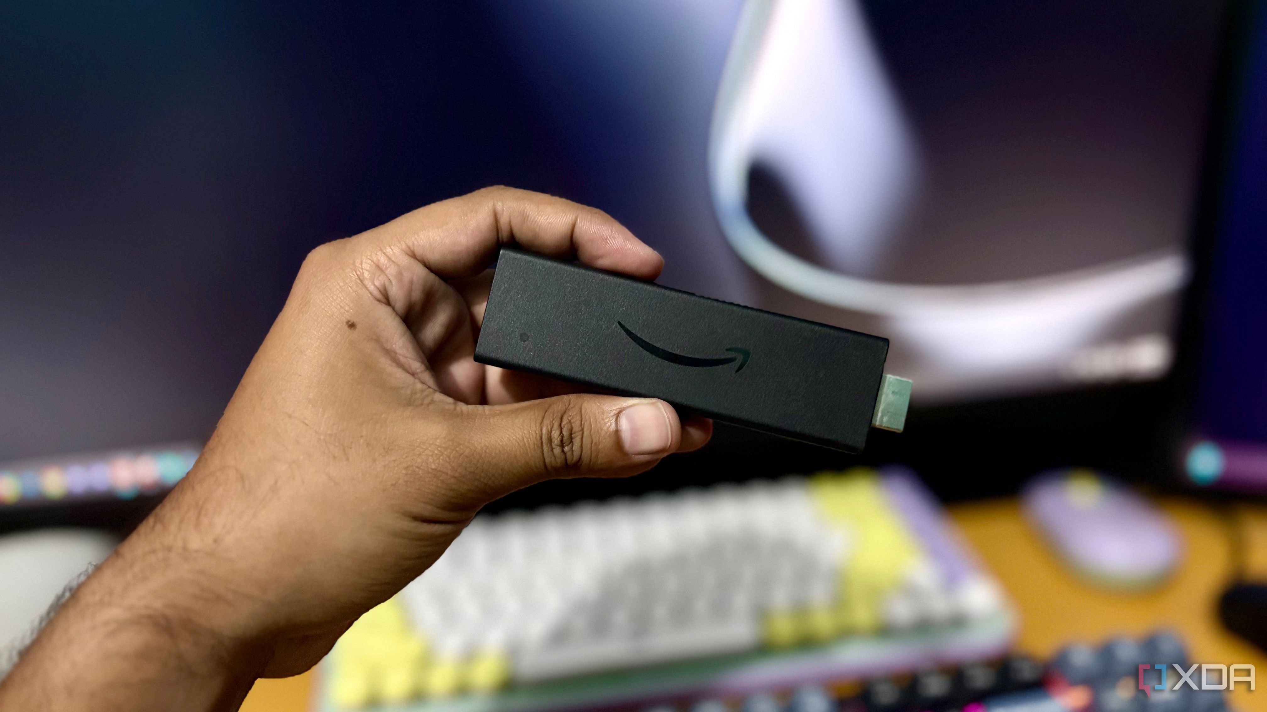 Amazon Fire TV Stick held in hand in front of a desktop setup