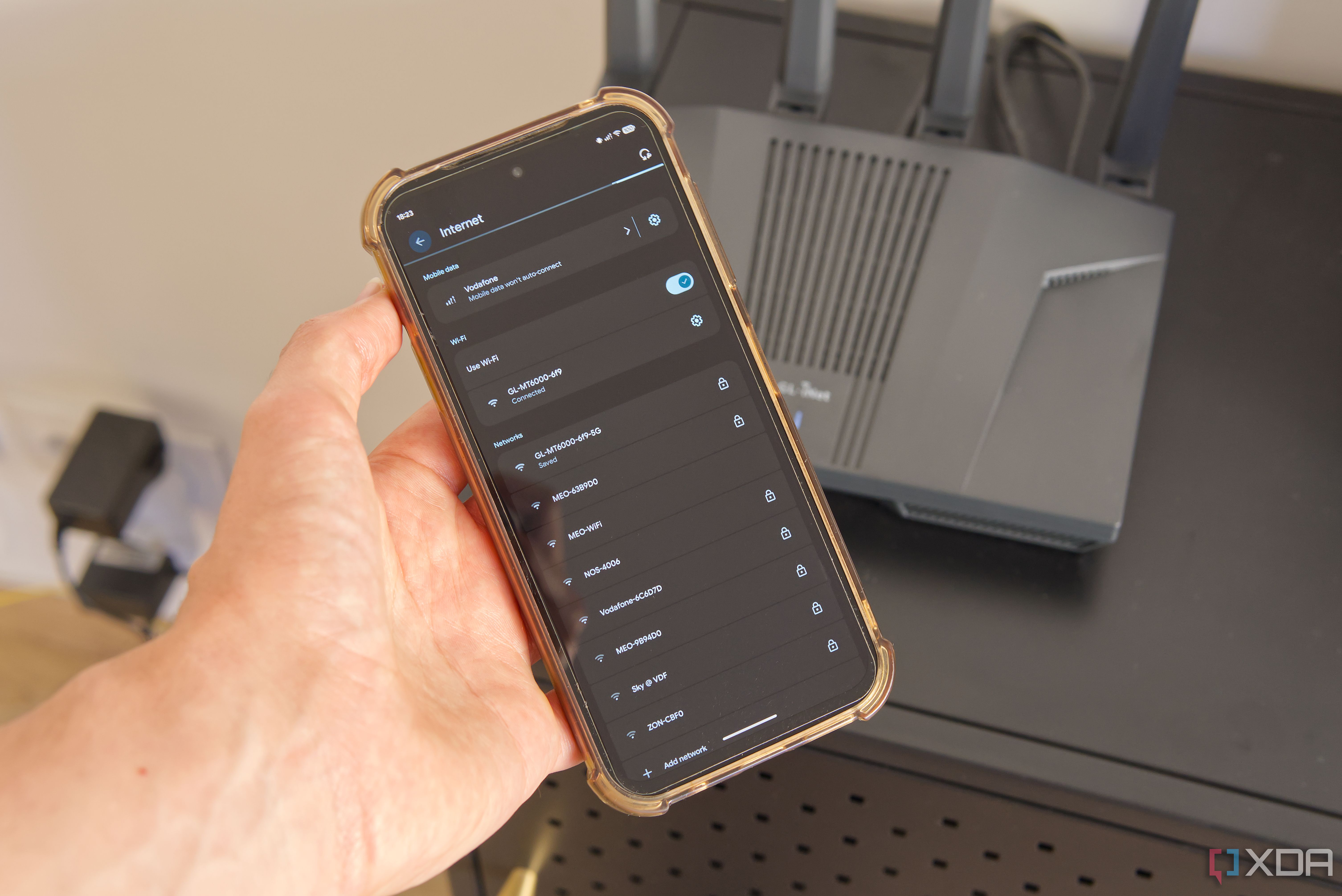 A smartphone showing a list of Wi-Fi networks with a router in the background
