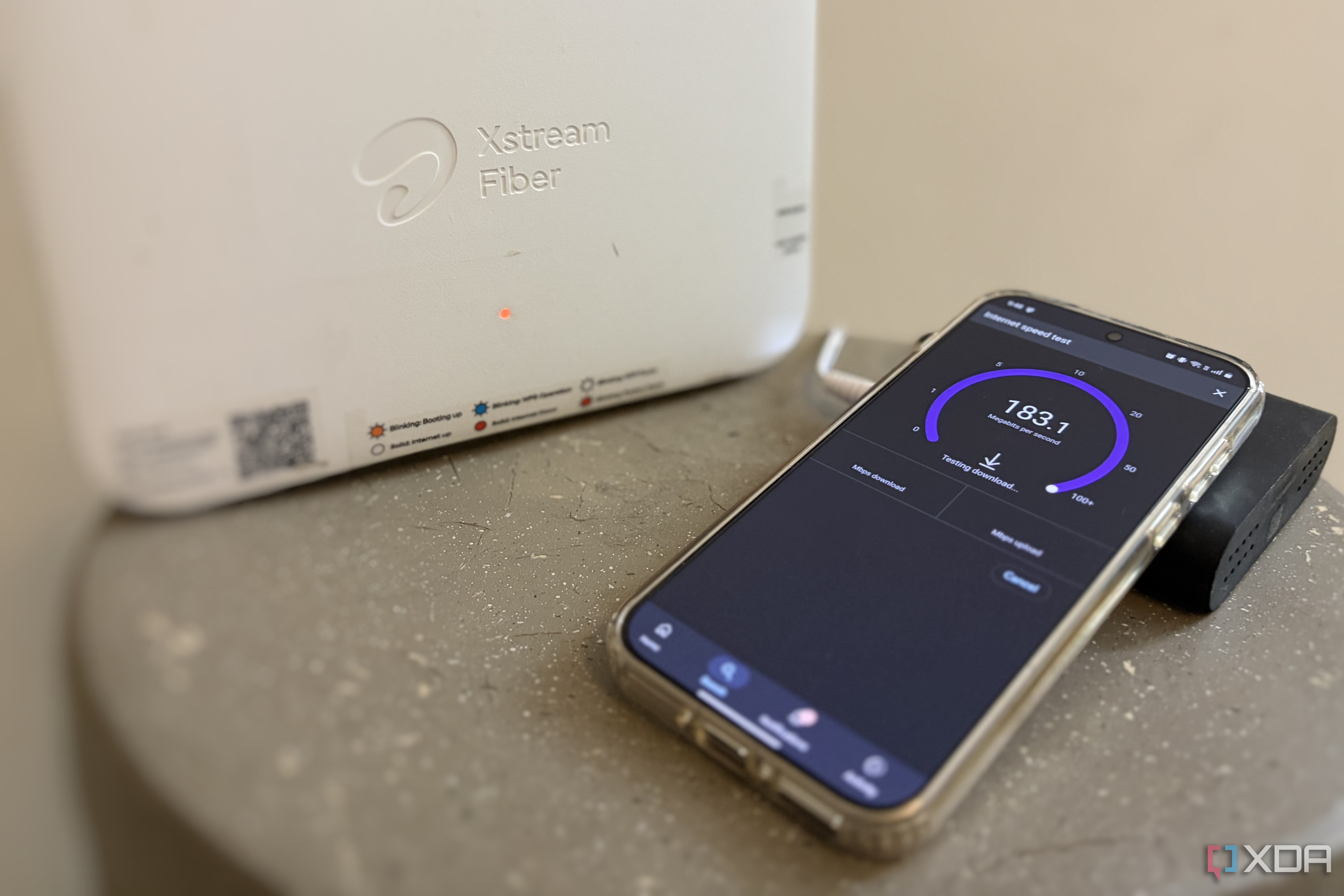 A smartphone running a Wi-Fi speed test next to a white router