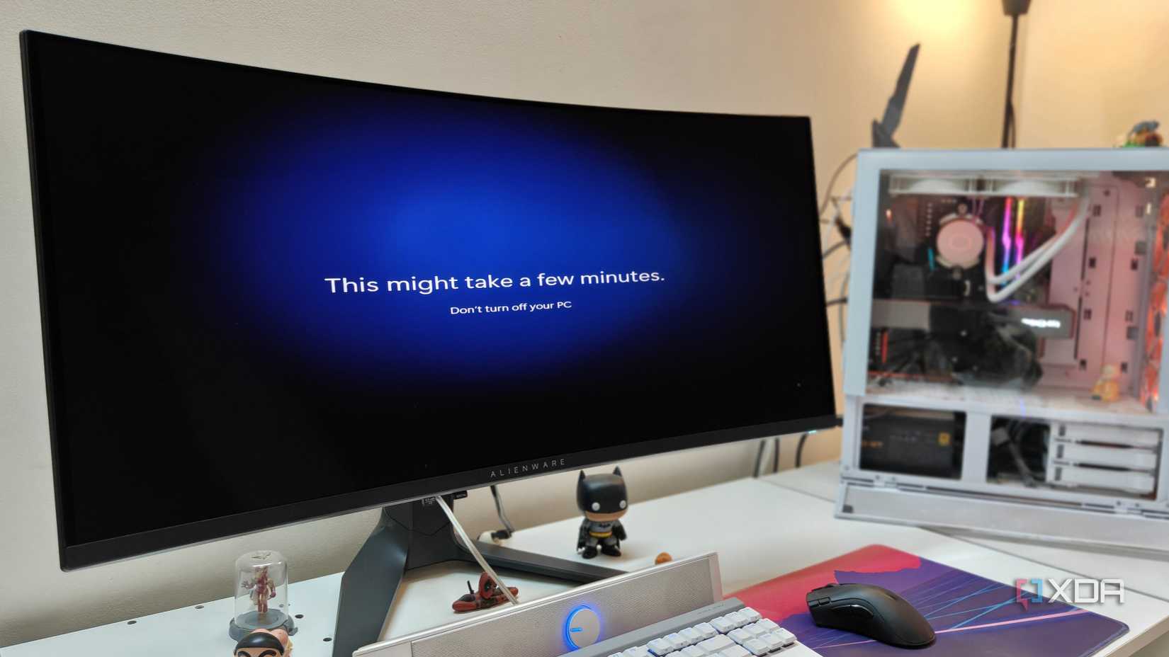 An ultrawide monitor showing Windows 11 settings with a gaming PC in the background