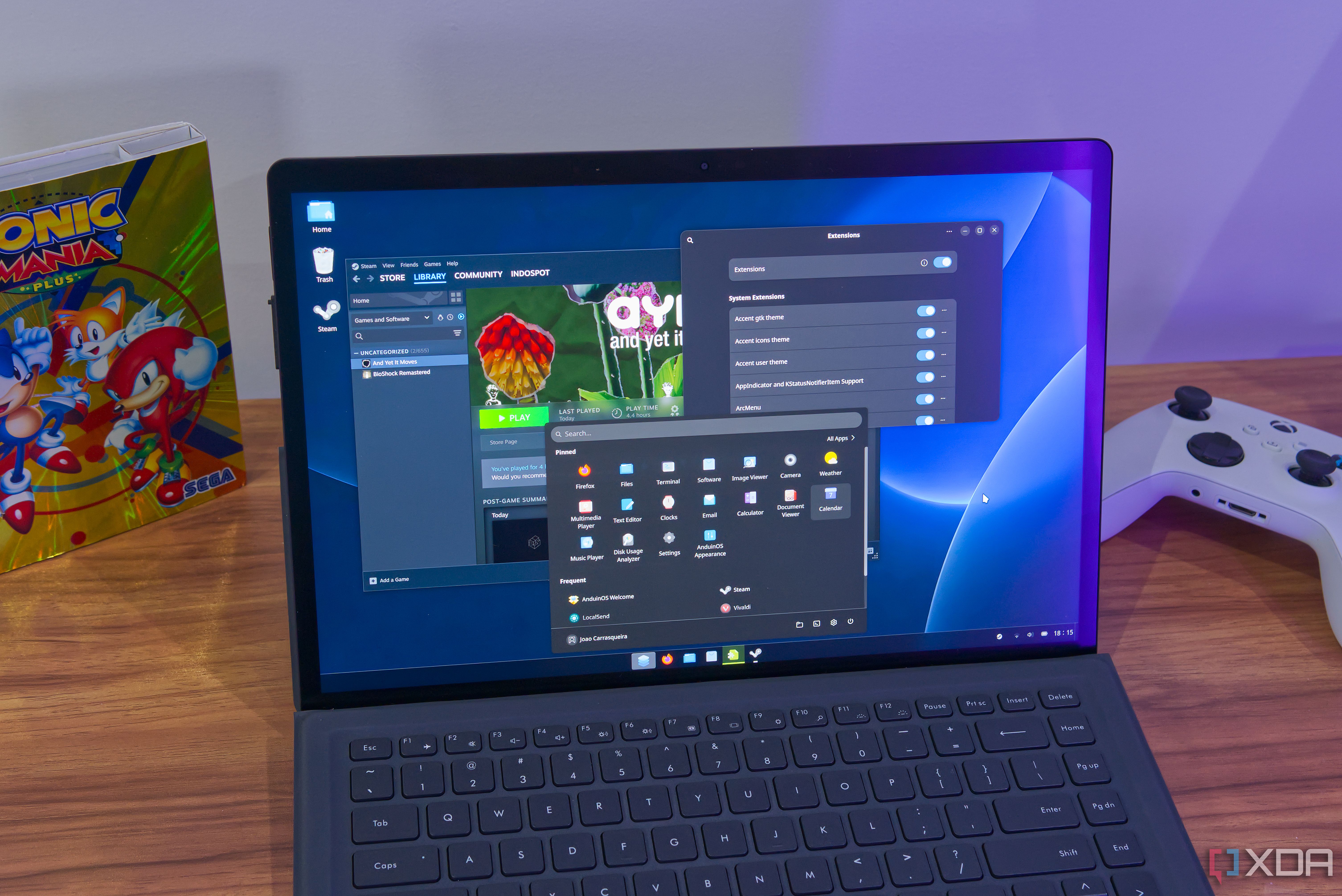 A 2-in-1 laptop running AnduinOS showing the ArcMenu app launcher, the GNOME Extensions app, and Steam on the desktop