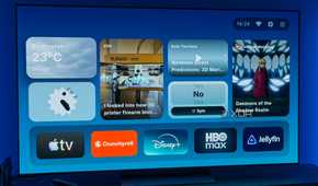 A TV displaying the homepage for AT4K Launcher for Android TV, with a small weather widget, a small analog clock widget, one full-size RSS feed widget for XDA, a small podcast widget, a small "Yes or no" spinner, and a "continue watching" card