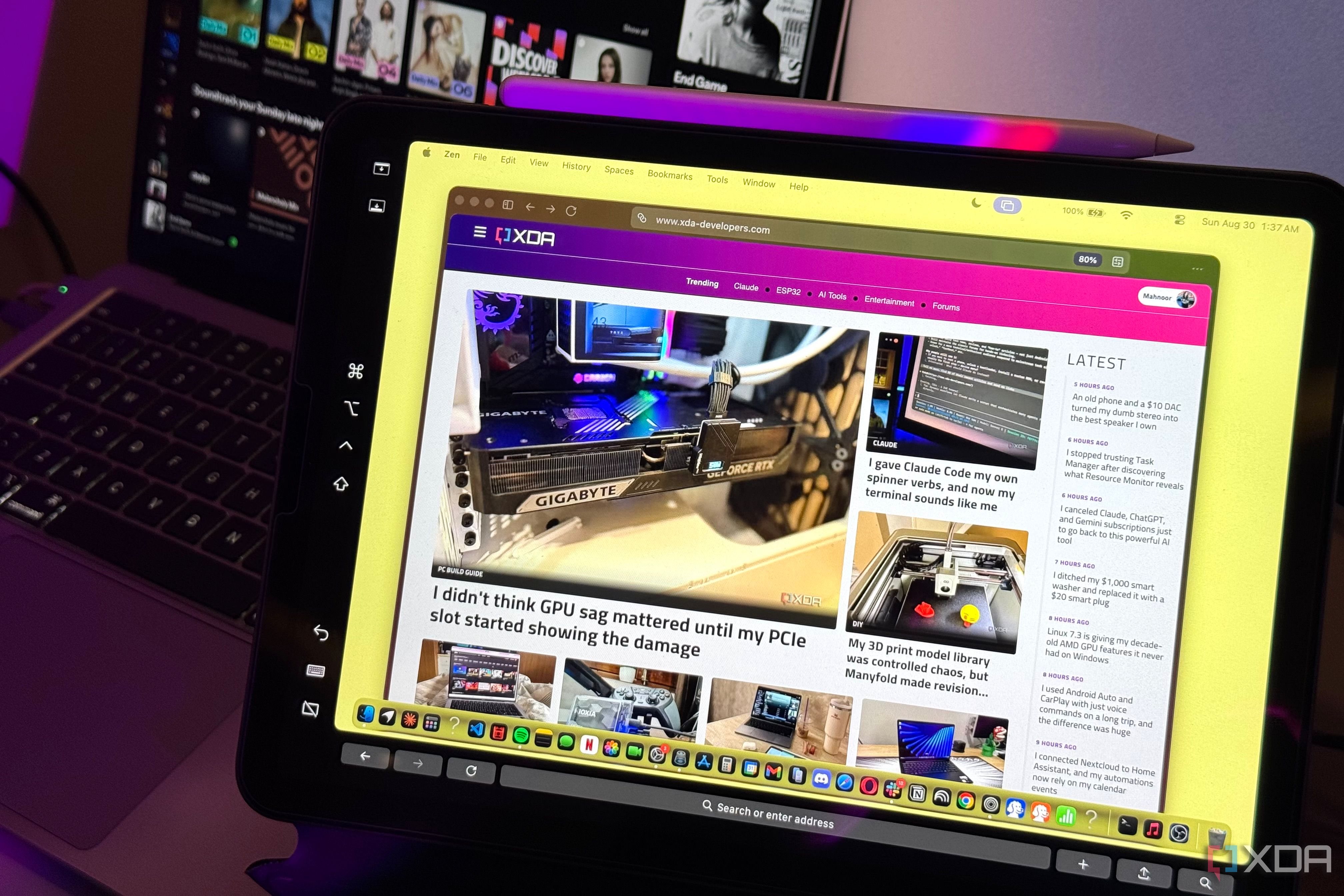 iPad running macOS-style Zen browser on the XDA Developers homepage, Spotify on the screen behind